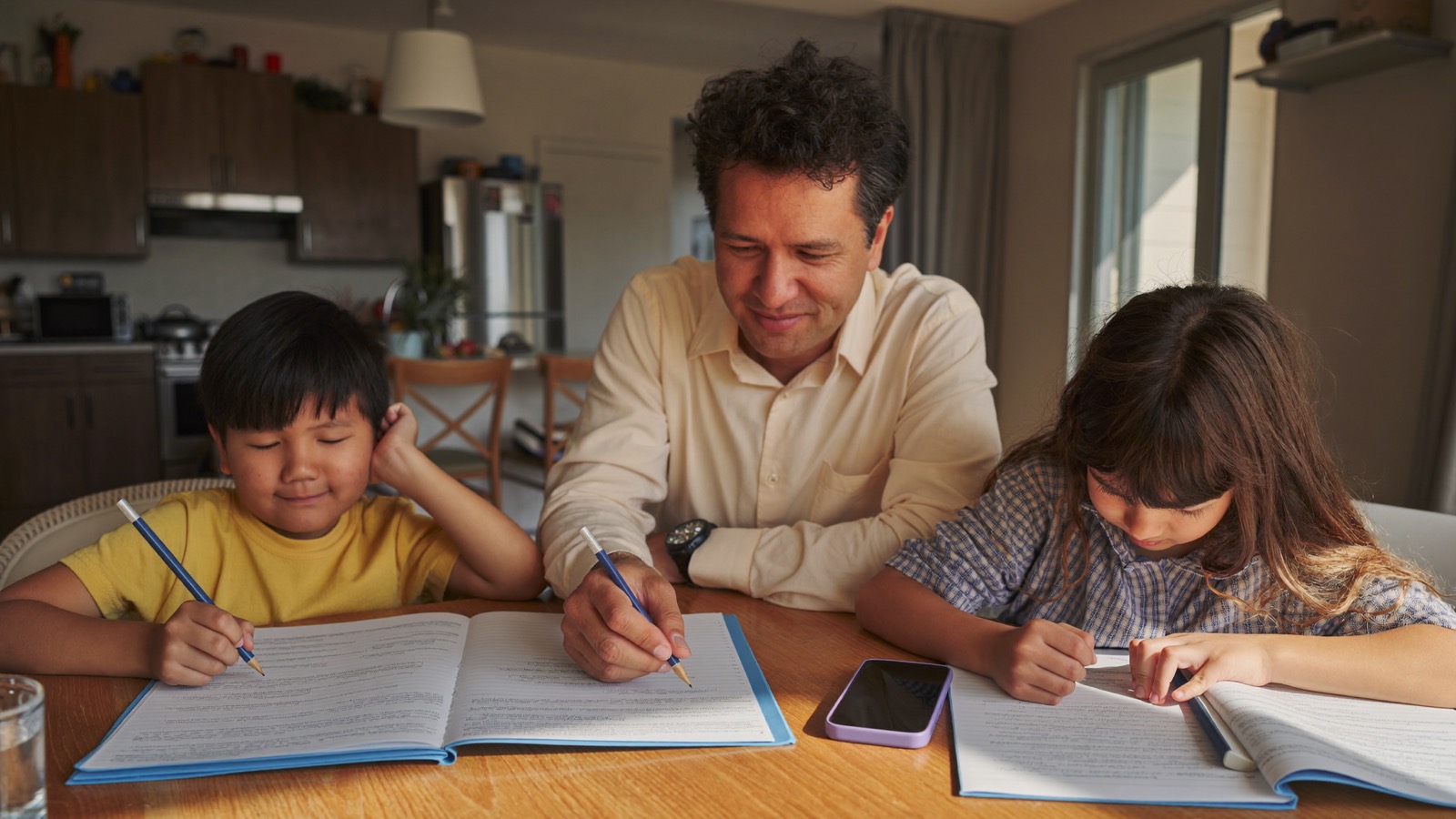 Un padre ayuda a sus dos hijos con las tareas en la mesa de la cocina